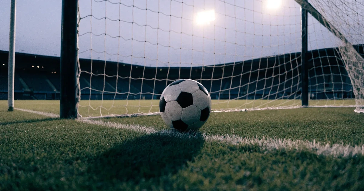 Ein Fußball liegt im Strafraum direkt vor dem Tor mit Netz, im Hintergrund leere Ränge bei Dämmerung.