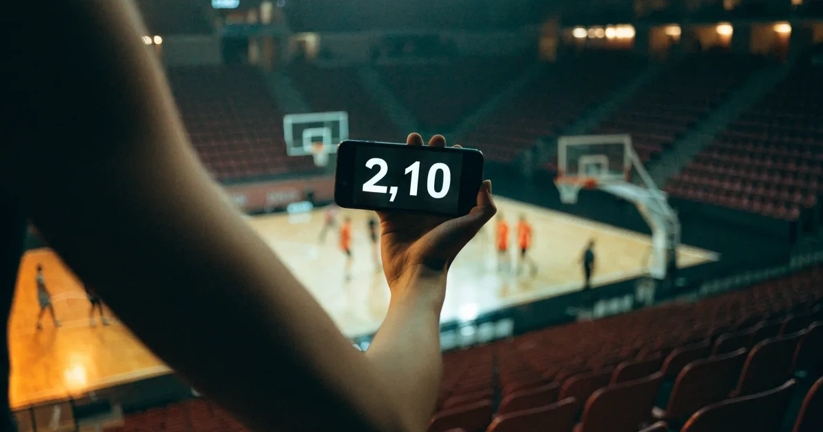 Eine leere Basketballhalle von einer oberen Tribünenreihe aus gesehen, Parkett und Körbe im Licht der Hallenstrahler.