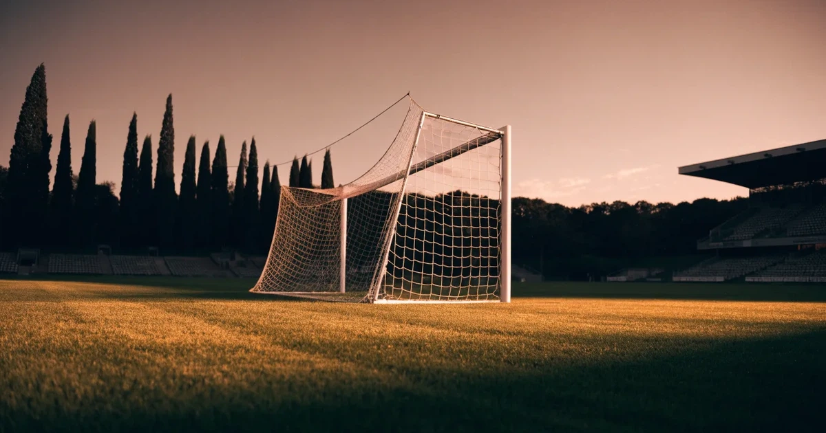 Ein Fußballtor mit Netz auf einem leeren Platz im Abendlicht, der Rasen frisch gemäht, im Hintergrund Zypressen.