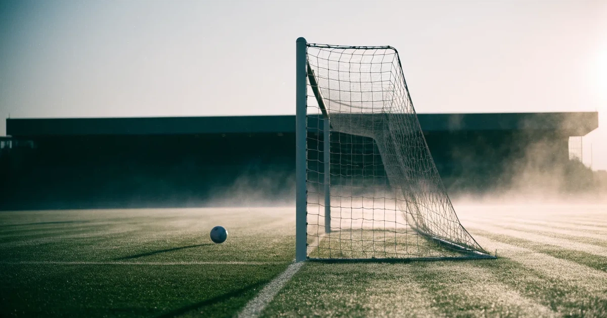 Ein Fußballtor mit Netz steht auf einem leeren Platz im Nebel der Morgendämmerung, der Rasen ist taufeucht.