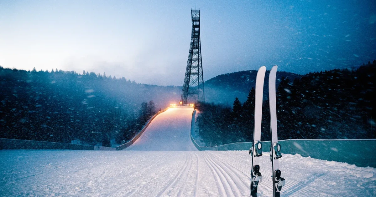 Eine Skisprungschanze im Schnee, von unten gesehen, vor einem klaren Winterhimmel in der Dämmerung, ohne Menschen.