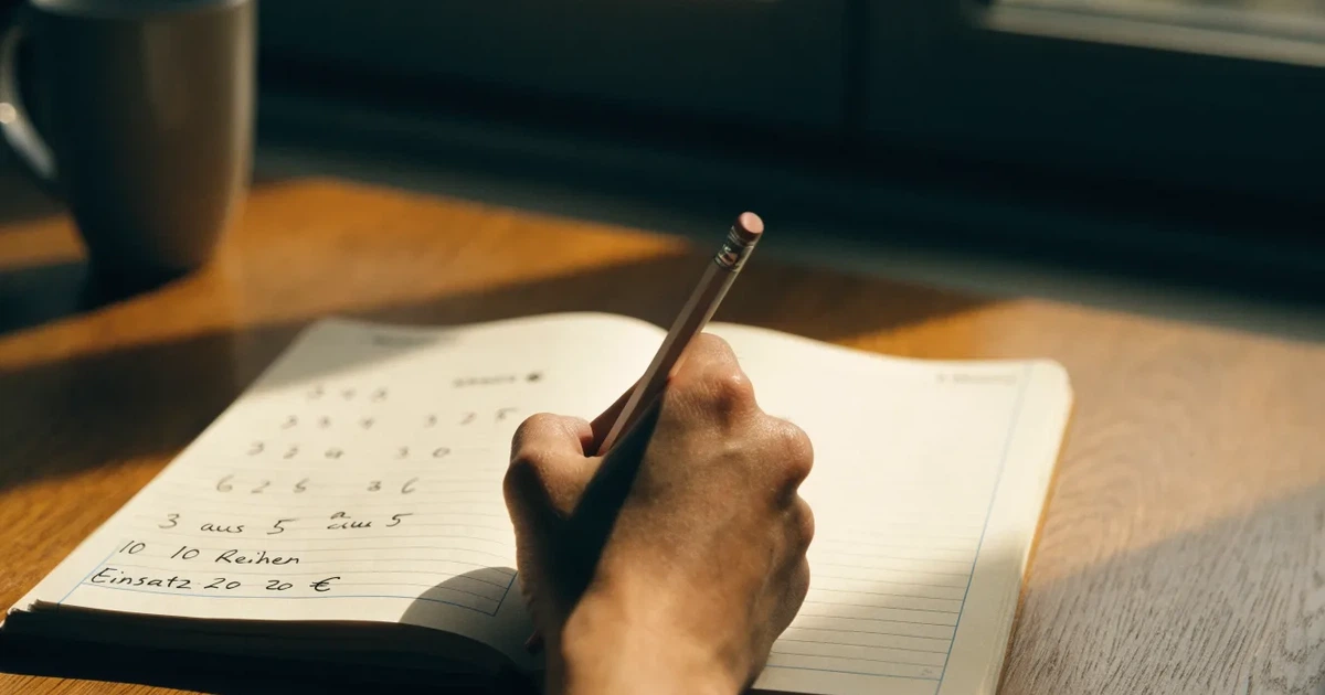 Ein Notizbuch mit handschriftlichen Notizen und einem Bleistift liegt neben einem Taschenrechner auf einem aufgeräumten Schreibtisch.