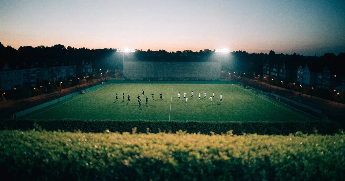 Ein Fußballstadion in der Dämmerung aus der Ferne, die Flutlichter gerade eingeschaltet, davor ein Kreisverkehr mit Laternen.